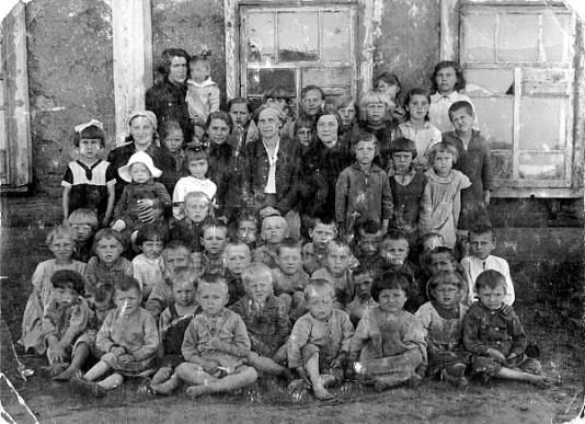 Grupa polskich dzieci oraz opiekunowie przed drewnianym budynkiem ochronki w Bajanowie.